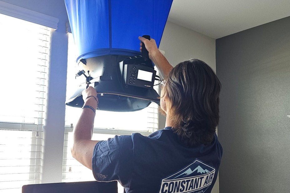 Constant Air Balancing technician using an ALNOR flow hood on a ceiling diffuser in a Las Vegas, NV home office