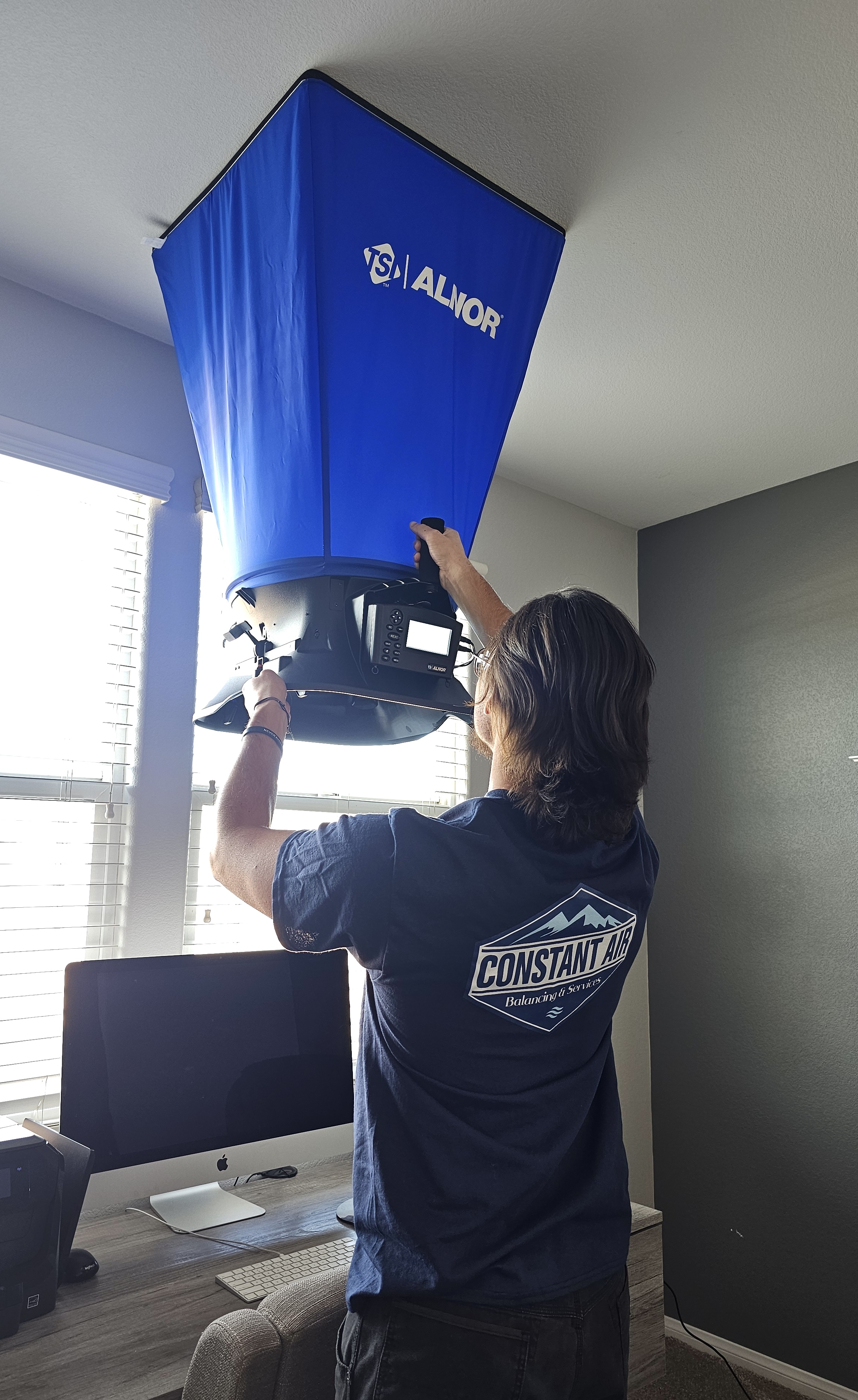 Constant Air Balancing technician using an ALNOR flow hood on a ceiling diffuser in a Las Vegas, NV home office
