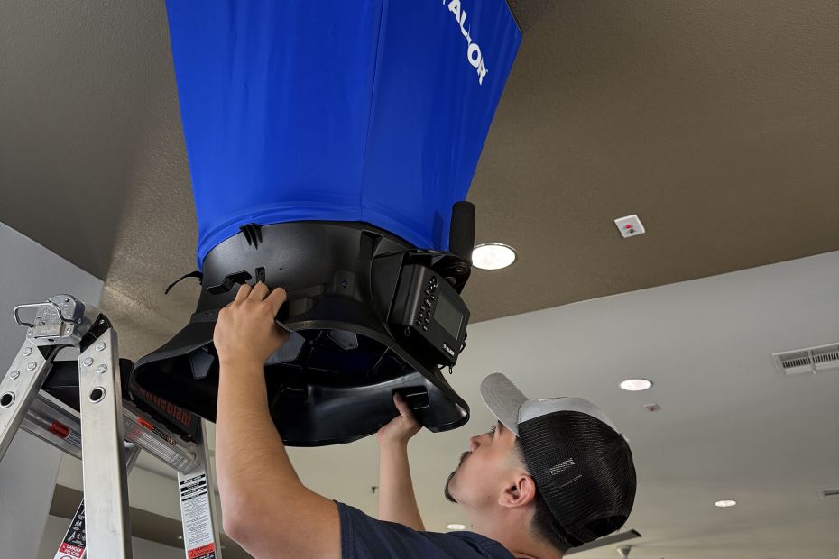 Constant Air Balancing technician on a ladder using an ALNOR flow hood on a commercial ceiling diffuser in Henderson, NV