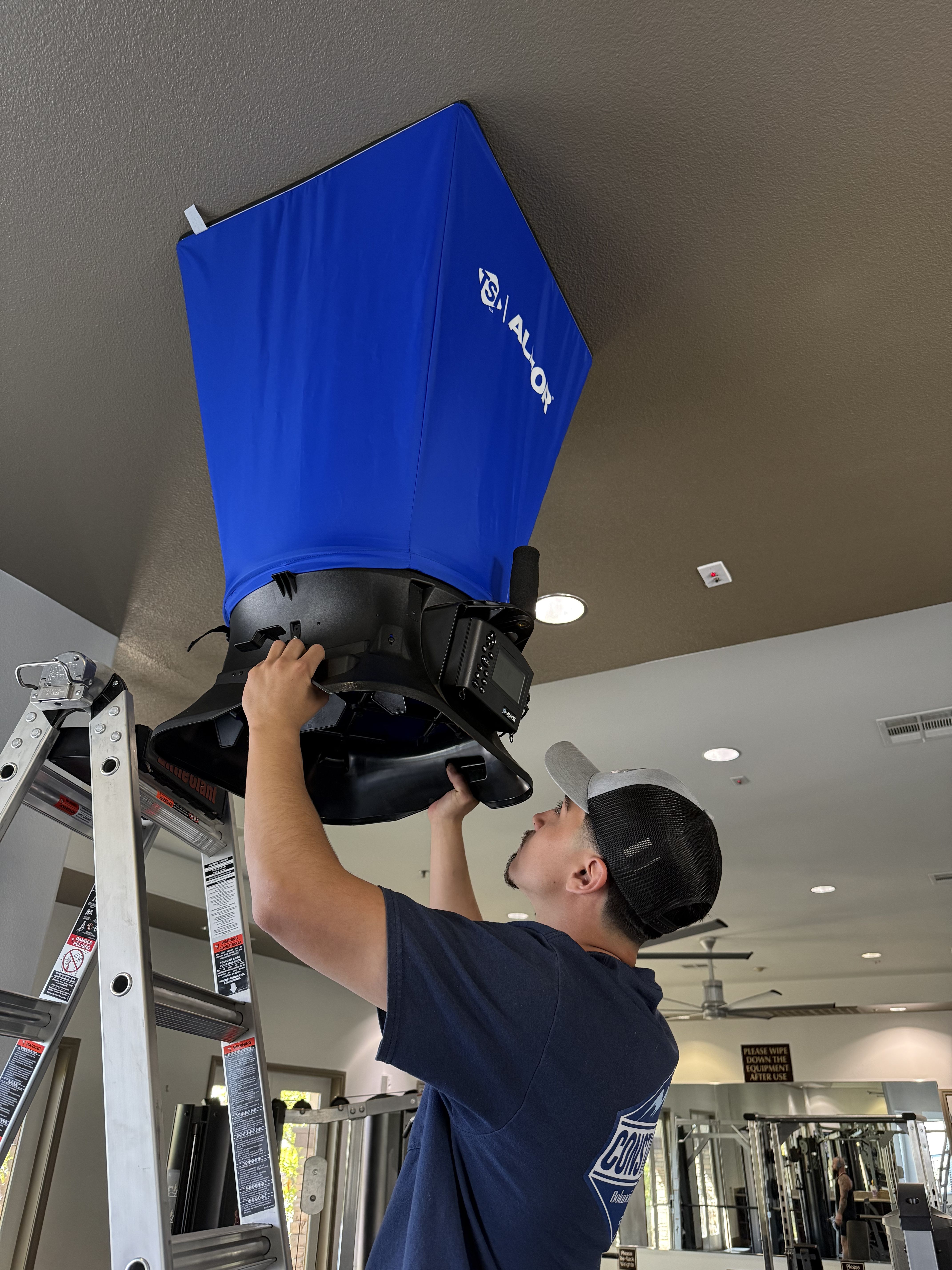 Constant Air Balancing technician on a ladder using an ALNOR flow hood on a commercial ceiling diffuser in Henderson, NV