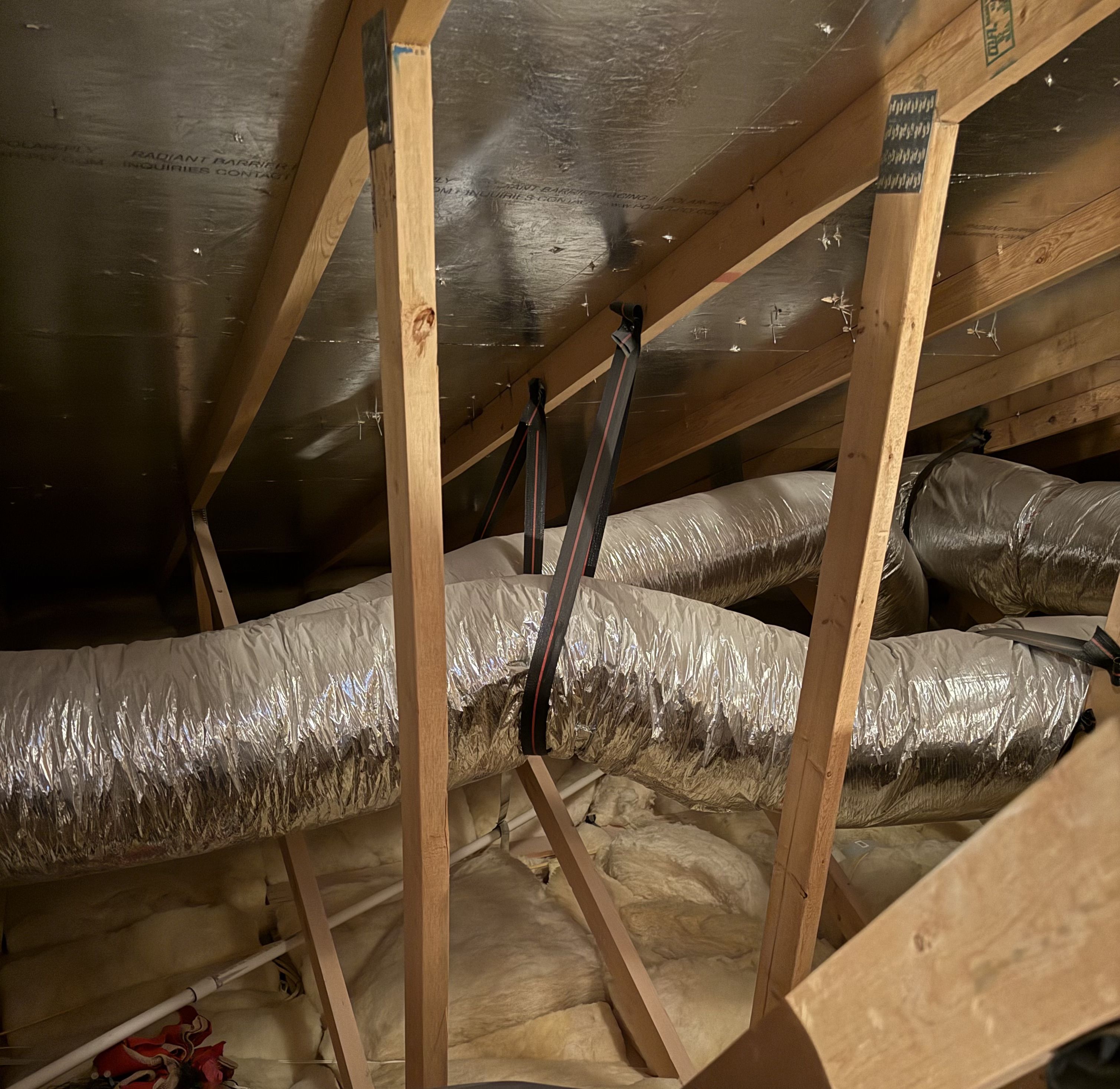 Insulated flex duct running through a hot attic above a Spring Valley home where leaks pull attic dust into the supply
