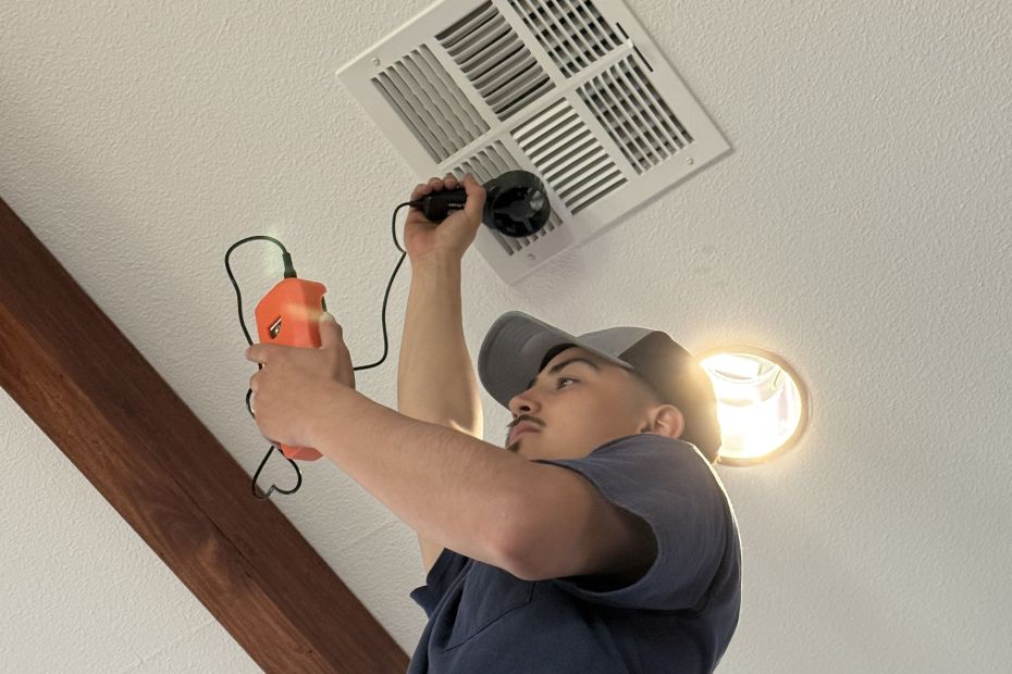 Constant Air Balancing technician measuring airflow at a ceiling register with an anemometer in a Las Vegas, NV home