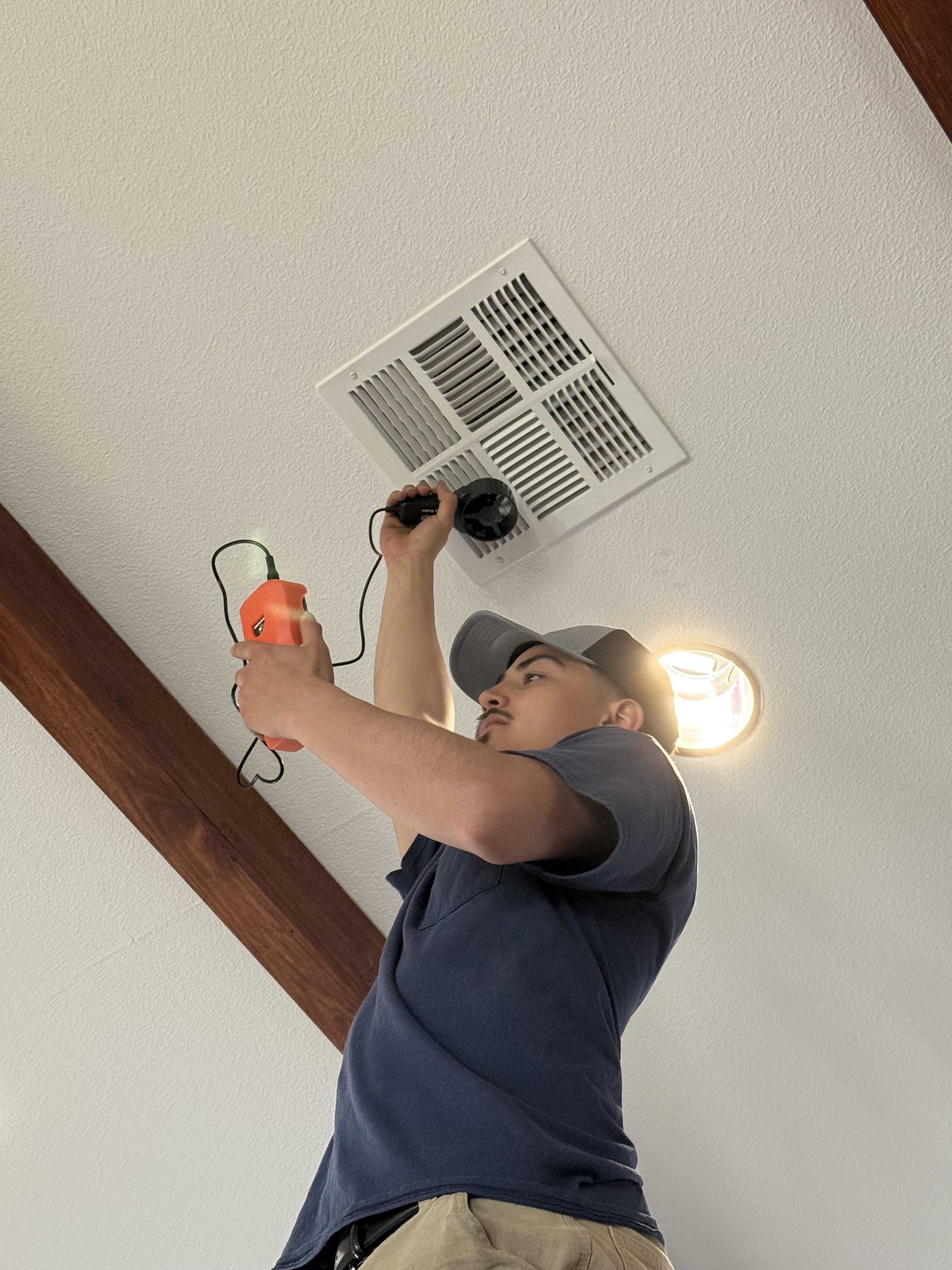 Constant Air Balancing technician holding an anemometer at a ceiling register during a Spring Valley airflow measurement