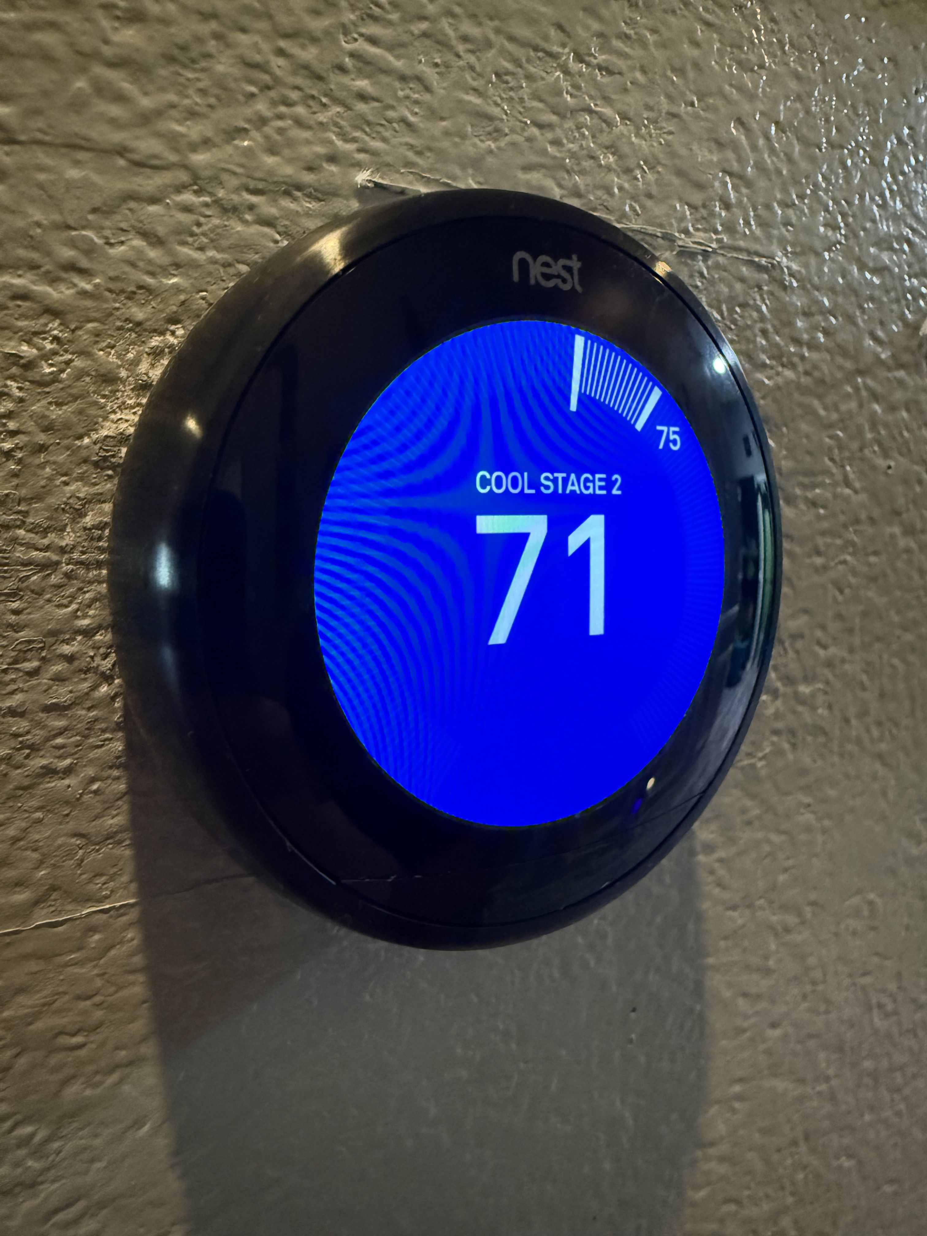 A round Nest thermostat mounted on a wall reading 71 degrees